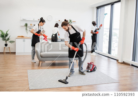 Multinational group of cleaners cleans bright studio kitchen. Multinational group of cleaners cleans bright studio kitchen. 110592393