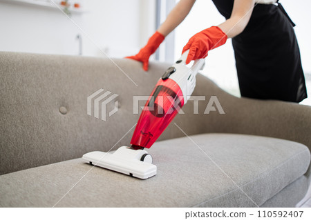 Close up view of hands of cleaner vacuuming sofa with portable vacuum cleaner. Close up view of hands of cleaner vacuuming sofa with portable vacuum cleaner. 110592407