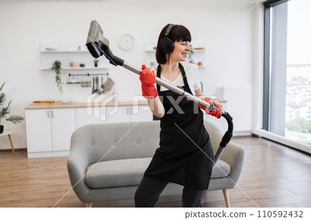 Positive young cleaners vacuuming rug of stylish modern studio kitchen. 110592432