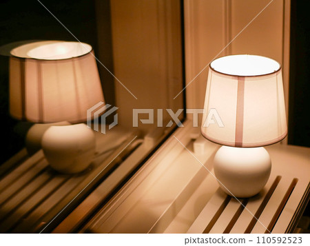 Image of Night lamp and reflection in window of a hotel room on the white wooden radiator cover 110592523