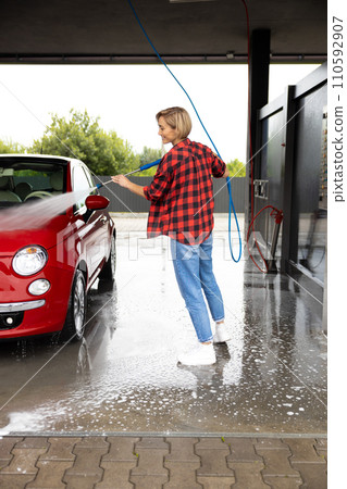 Young blonde woman washing the car with a hose 110592907