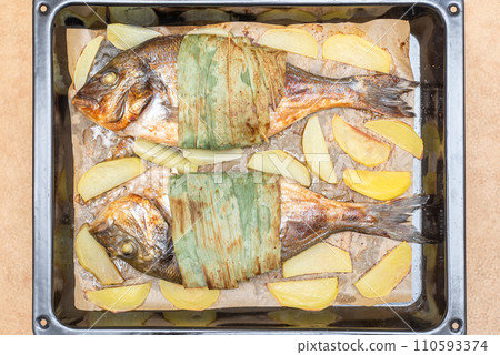 Top view of baked dorado fish and potatoes on a baking sheet. 110593374