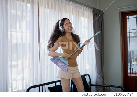 Asian woman dancing while cleaning in the house. 110593784