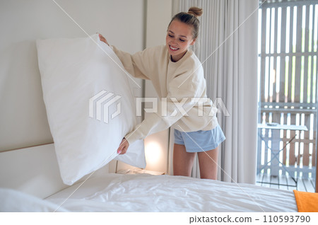 Beautiful woman putting on fresh bed linen in hotel room. 110593790
