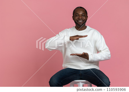 Cheerful black man wearing white sweatshirt showing empty space with hands big size 110593906