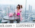 Stylish woman in beautiful fashion pink blazer with cute bag holding mobile phone on rooftop terrace with amazing Bangkok view high floor industrial city 110594037