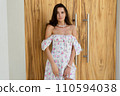 Young beautiful woman in a romantic dress with a floral print, and a pearl necklace bracelet, against the background of a wooden door 110594038