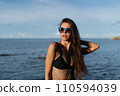 Young beautiful tanned woman on the background of the sea at sunset in a black swimsuit and a mesh dress 110594039