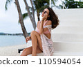 Stylish young woman with voluminous hair in a bikini and lace pareo posing on a tropical beach, slim, tanned, athletic, sunglasses 110594054