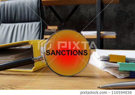 Office table with contracts and a magnifying glass with the inscription sanctions. Office table with contracts and a magnifying glass with the inscription sanctions. 110594836