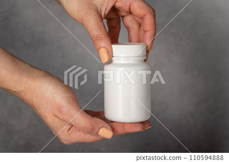 Female hand holding a white plastic bottle with pills. Beauty care capsules, collagen, vitamins 110594888