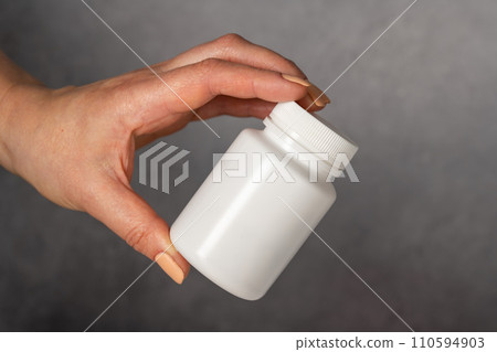 Female hand holding a white plastic bottle with pills. Capsules, collagen, vitamins, pain killers or drugs Female hand holding a white plastic bottle with pills. Capsules, collagen, vitamins, pain killers or drugs 110594903