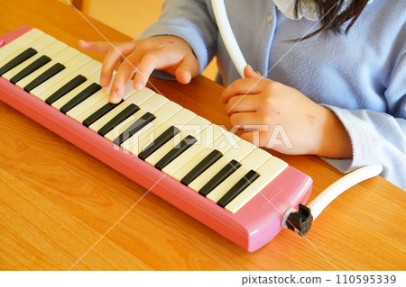 一名小學四年級的女孩正在吹鍵盤口琴。 一名小學四年級的女孩正在吹鍵盤口琴。 110595339