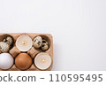 Eggs and candle in eggshell in tray on white background. Quail and chicken eggs. Copy space. Easter holiday concept 110595495