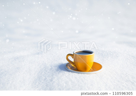 Winter background. Yellow cup with hot coffee or tea stands on the snow outdoor at sunny day with cold weather outdoors. 110596305