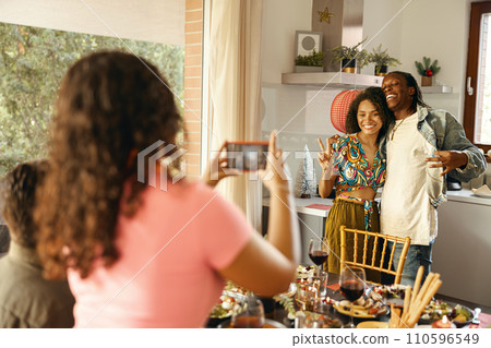 Back view of woman making photo on phone for smiling friends couple during festive home party 110596549