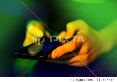 Using mobile in female hand close up on a neon glowing background Using mobile in female hand close up on a neon glowing background 110596732