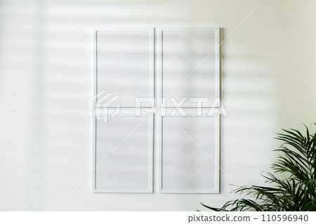 Blank white frames and houseplant against white wall 110596940