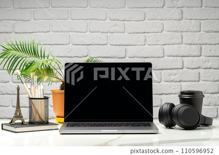 Laptop with black screen on desk against white brick wall Laptop with black screen on desk against white brick wall 110596952