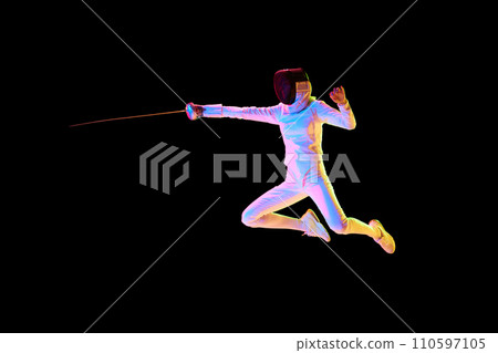 A fencer in full gear lunging with precision, isolated on black background in neon. Female athlete in motion, training with sword. 110597105