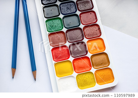 Colorful watercolor or acrylic paints and pencils on a white sheet of paper on a white background. Design studio table top view.  110597989