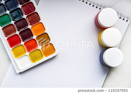 Colorful watercolor or acrylic paints and pencils on a white sheet of paper on a white background. Design studio table top view. Space for text. Colorful watercolor or acrylic paints and pencils on a white sheet of paper on a white background. Design studio table top view. Space for text. 110597993