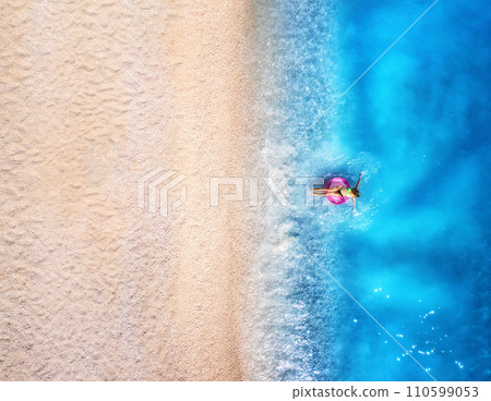 Aerial view of a woman with swim ring in blue sea, sandy beach 110599053