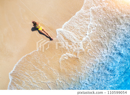 Aerial view of the young lying woman on the sandy beach near sea Aerial view of the young lying woman on the sandy beach near sea 110599054