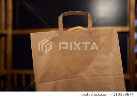 Craft paper bag on a wooden table against a brick wall. Takeaway food packaging rustic template 110599674