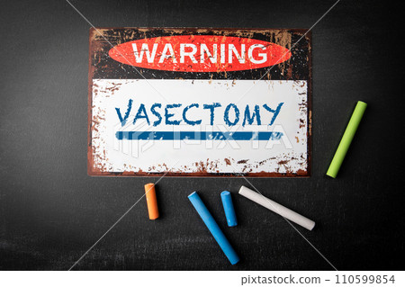 VASECTOMY. Metal warning sign and colored pieces of chalk on a dark chalkboard background VASECTOMY. Metal warning sign and colored pieces of chalk on a dark chalkboard background 110599854