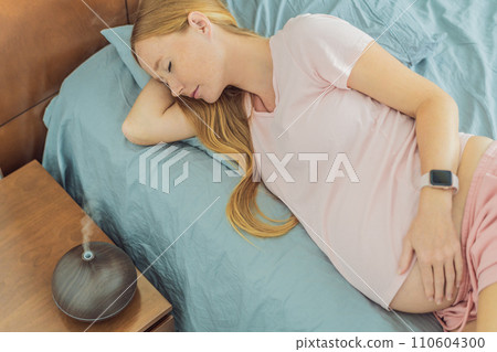 Expectant woman finds relaxation in bed, embracing tranquility with the help of an aroma diffuser during a moment of rest 110604300
