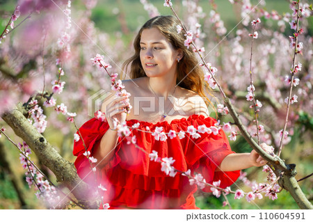 Woman in red dress standing near blooming peach tree 110604591
