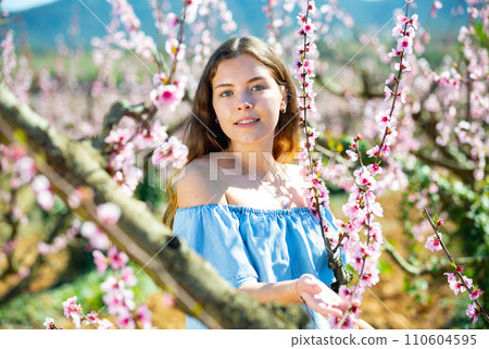 Beautiful blonde girl with long hair in a pink dress in blooming garden. 110604595