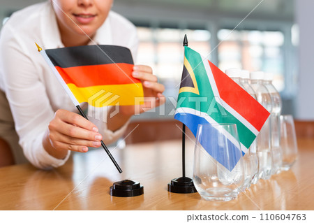 Little flag of South Africa on table and flag of Germany put next to it by young woman 110604763