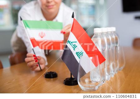 Woman secretary prepares an office for negotiations - she places flags of Iraq and Iran table Woman secretary prepares an office for negotiations - she places flags of Iraq and Iran table 110604831