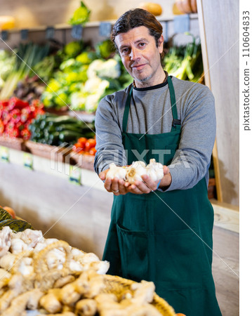 Male seller holding garlic standing in fruit and vegetable section of supermarket Male seller holding garlic standing in fruit and vegetable section of supermarket 110604833