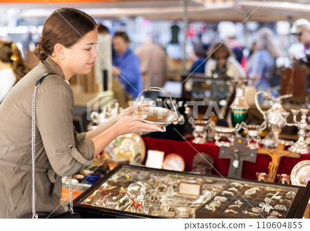 Satisfied young woman choosing interesting antique things at traditional flea market Satisfied young woman choosing interesting antique things at traditional flea market 110604855