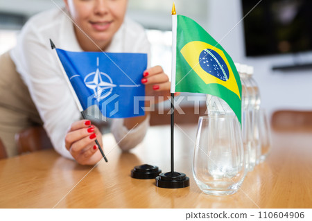 Little flag of Brazil on table and flag of NATO put next to it by young woman 110604906