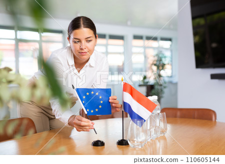 Young woman puts EU and Netherlands flags on table in office 110605144