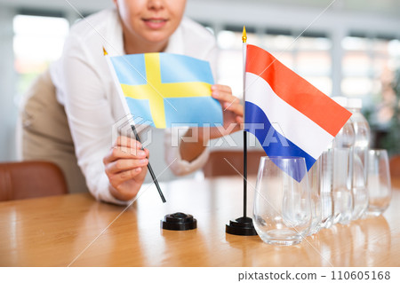 Young woman putting flags of Sweden and Netherlands on table in office Young woman putting flags of Sweden and Netherlands on table in office 110605168