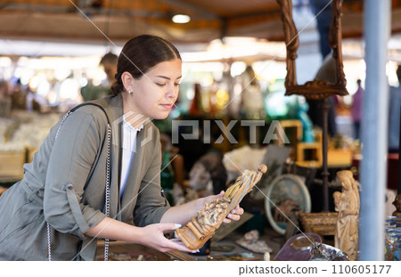 Happy female tourist looking to buy handmade wooden statue at flea market Happy female tourist looking to buy handmade wooden statue at flea market 110605177