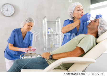 Woman cosmetologist making injections between eyebrows to male patient Woman cosmetologist making injections between eyebrows to male patient 110605199