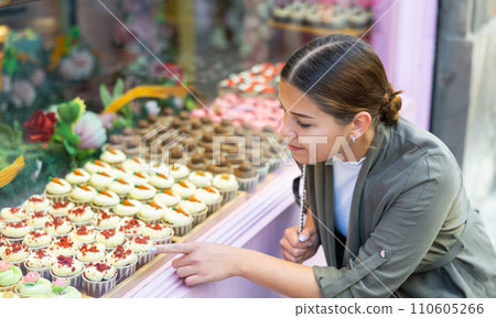 Satisfied woman at the shop window chooses sweet muffins and cakes 110605266