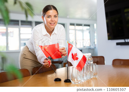 Young woman putting flags of China and Canada on table in office Young woman putting flags of China and Canada on table in office 110605307