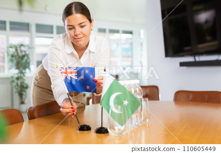 Positive young woman putting little flag of Australia on table next to the flag of Pakistan 110605449