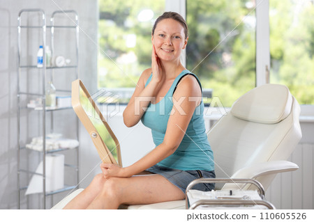 Young woman holds mirror in hands and admires reflection in comsetological clinic 110605526