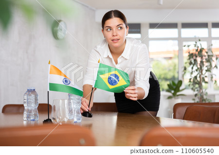 Young female attendant putting up flags for international negotiations between india and brazil 110605540