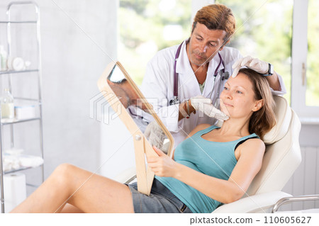 Woman looking at mirror while cosmetologist showing results of facial procedure Woman looking at mirror while cosmetologist showing results of facial procedure 110605627