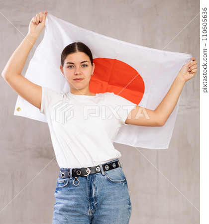 Serious young woman holding state flag of Japan against gray wall background indoors 110605636