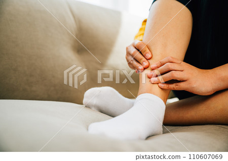 Illustrating health care concept, woman sits on sofa holding her painful ankle. Emphasizing varicose vein prevention leg recovery and pain management for the patient. medical 110607069